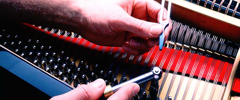 Hands tuning piano strings during a service visit
