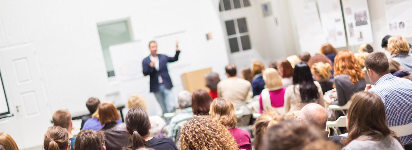 Man giving presentation in front of medium sized crowd indoors.