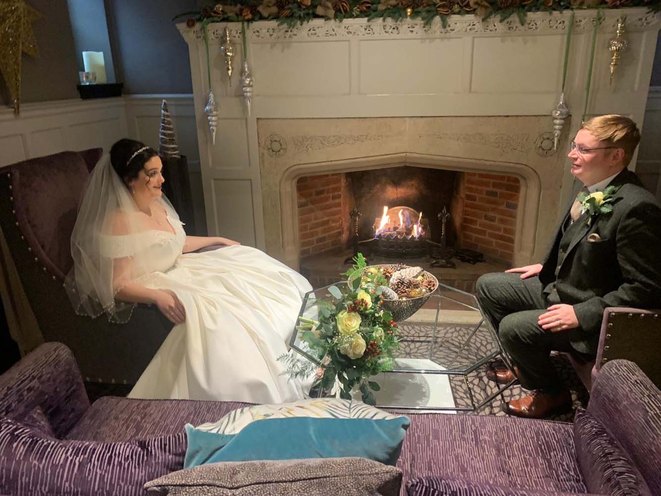 A bride and groom sitting infron of a roarng open fire.