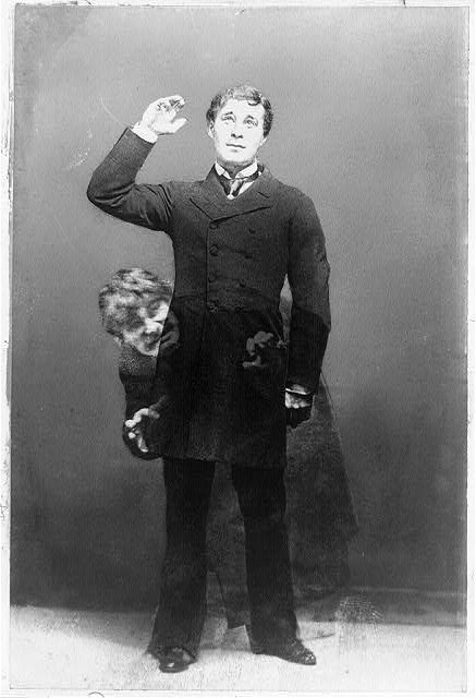 Distressed black and white image of man in trousers and a long buttoned jacket. A translucent alter ego appears bent over, looking angry or scared behind him. Almost coming out of him.