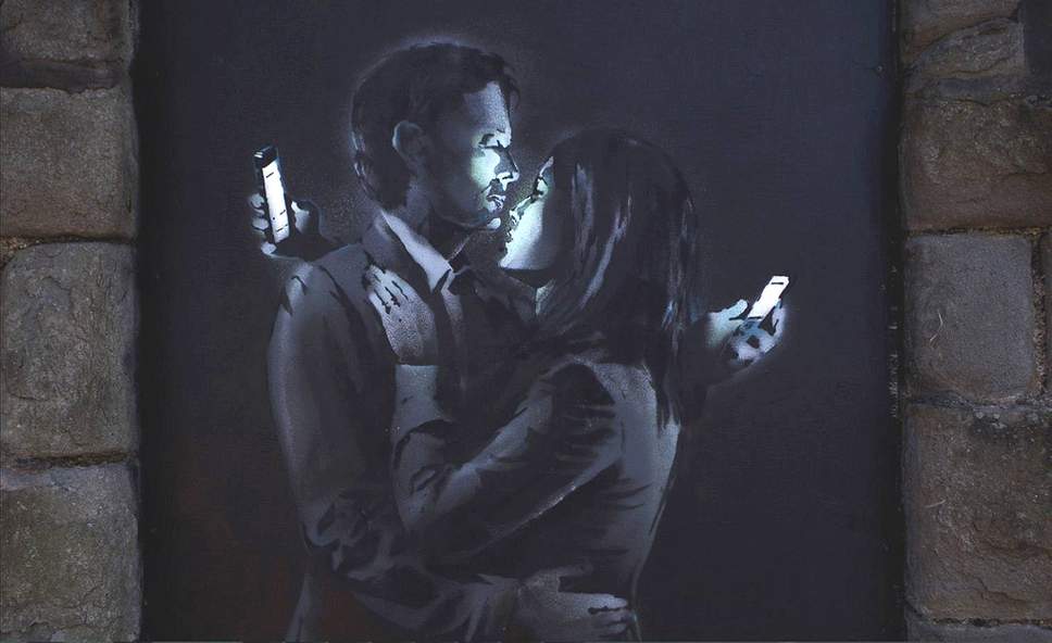 Parte de Banksy de um homem e de uma mulher que abraçam ao olhar seus telefones móveis.