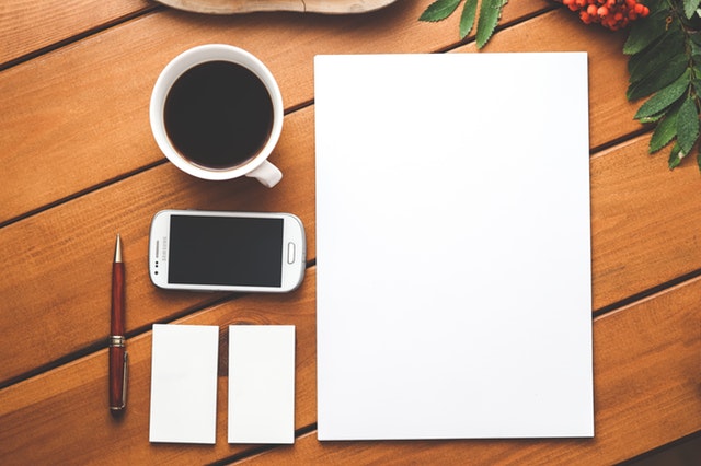 Blank flyers and business cards arranged on a table with coffee, a phone, and a pen.