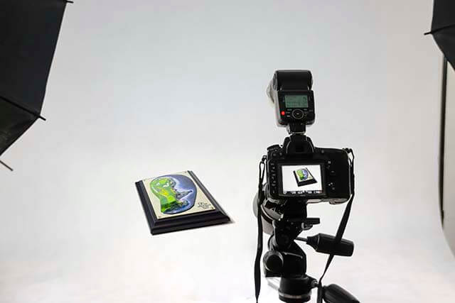 A camera is pointed at a small object on a white background, with lights visible in the corners of the scene.