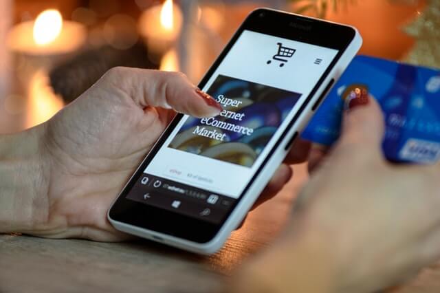 A woman holds a phone in one hand and a credit card in the other.