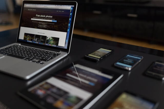 A laptop, tablet, and three mobile phones sit on a desk.
