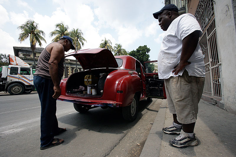 foto van twee mannen op straat in Cuba bij rode auto die de achterklep open heeft