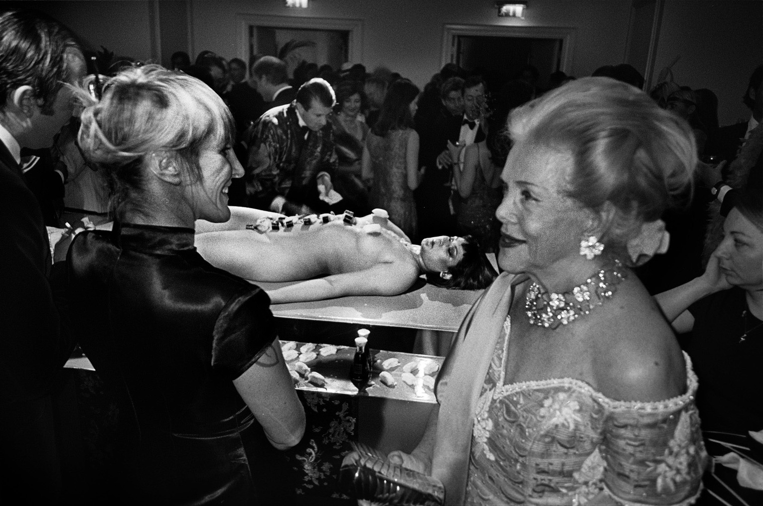 foto van rijke mensen met diamanten om op een feest waar in het midden een naakte vrouw ligt met stenen? op haar buik