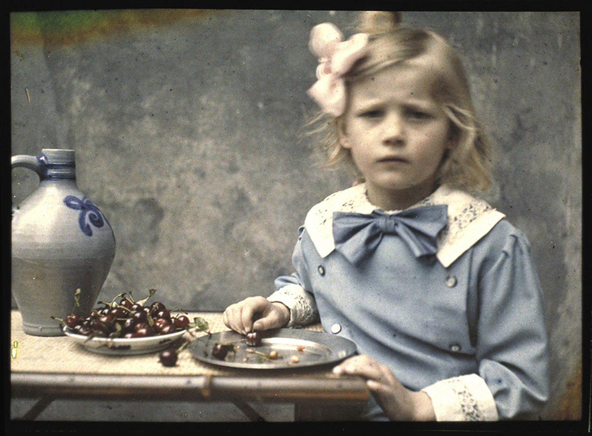foto van Marietje Zeegers, dochter van de fotograaf van rond 1900, waar ze aan een tafel met kersen zit