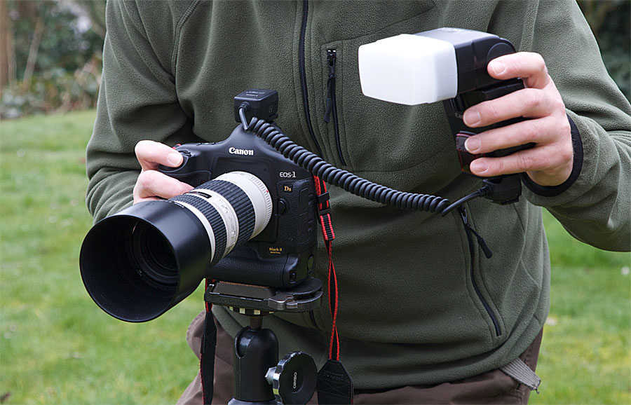 foto van camera met flitser via kabel vastgehouden door man