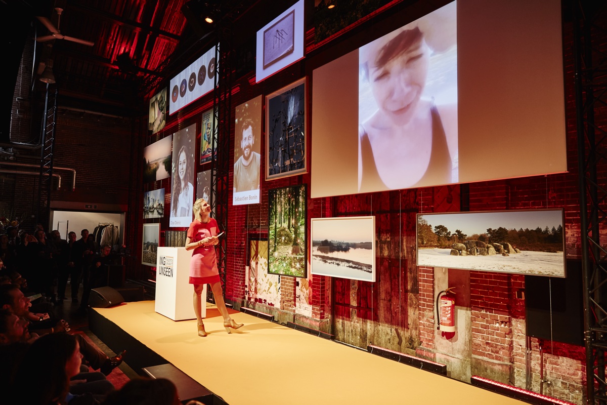foto van presentatie door vrouw in rode jurk met foto's op groot scherm van Unseen talent award 2015
