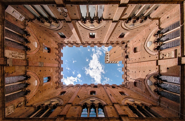 architectuurfoto van de binnenplaats van het Pallazzo Publico (Stadhuis) van Siena, Italië. Recht naar boven kijkend worden de patronen en symmetrie in de architectuur fraai benadrukt