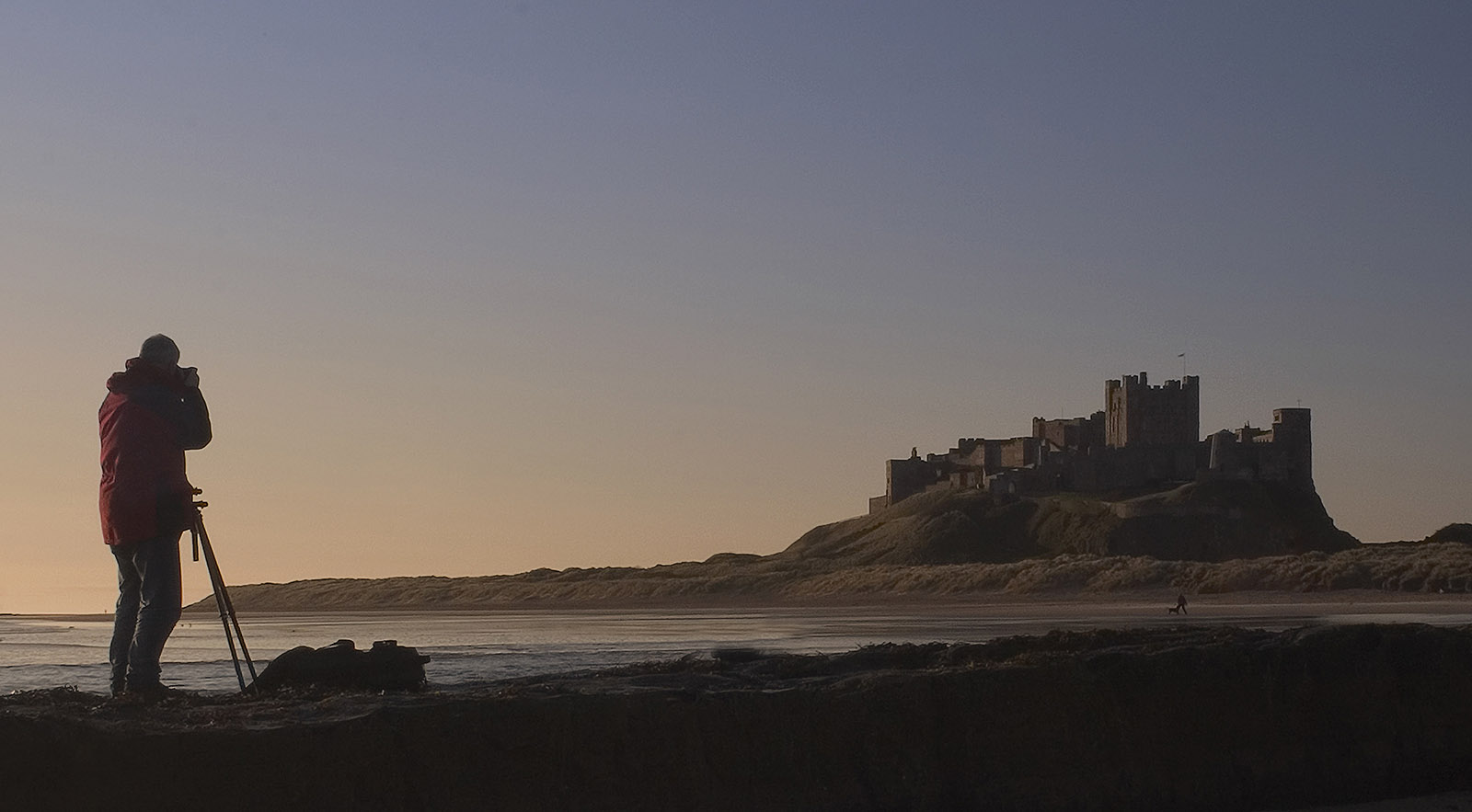 foto van man die foto maakt van oud kasteel op een berg bij de zee in avondlicht