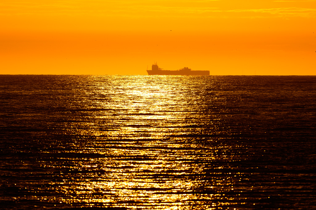 foto van zonweerspiegeling op zee met boot aan horizon en gele lucht