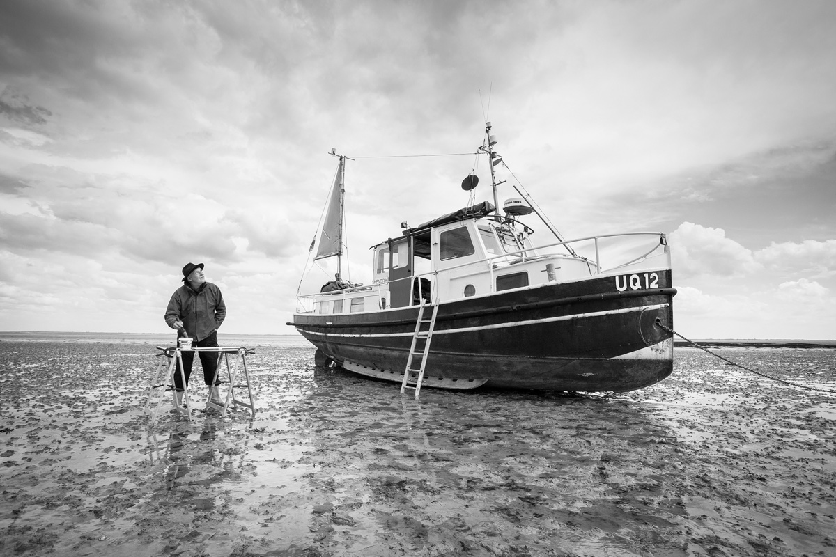 foto van waddenschilder op wadden met emmer verf en boot
