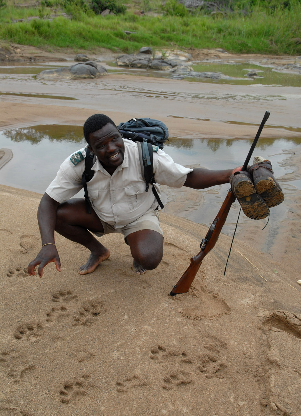 foto: Tom van der Leij van landschap Zuid-Afrika met reisgids geknield en met geweer in handen en schoenen uit in handen