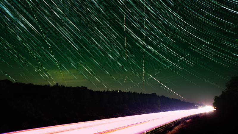 startrailfoto van weg met autolichten en in de lucht de strepen