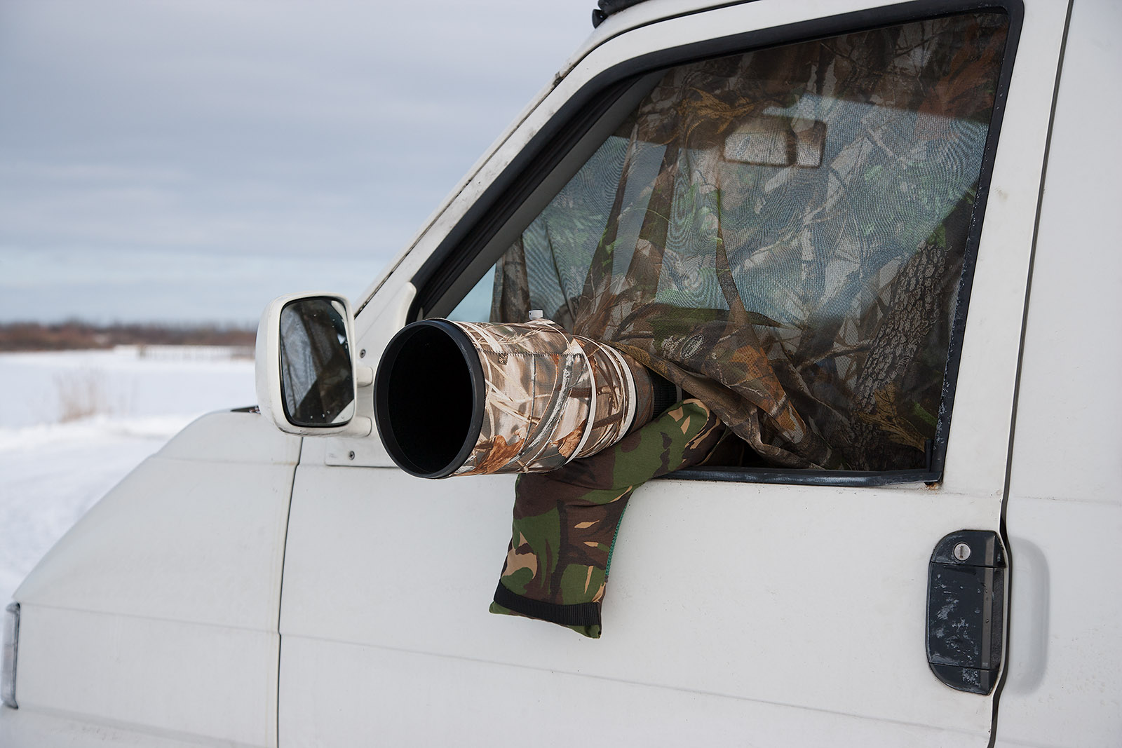 foto van wit busje met camouflagedoek voor het raam en een cameralens die uit voorraam steekt ook gecamoufleerd