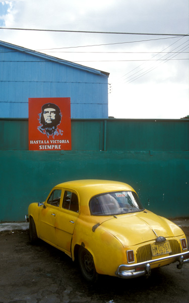 Polychroom kleurgebruik met felle drukke kleurvlakken:| gele cubaanse auto bij schutting met rood affiche
