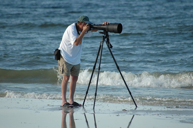 man met camera en telelens op statief bij branding zee