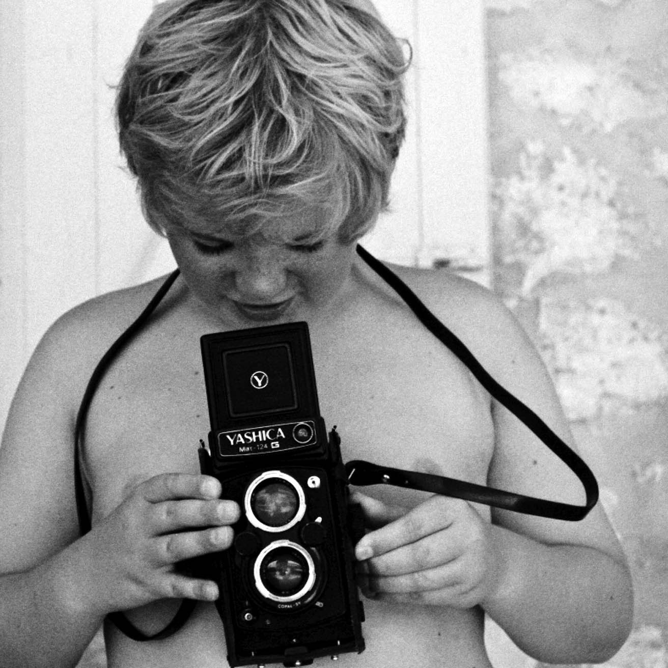 foto van een jongetje die in een analoge camera kijkt die hij voor zijn blote borst houdt