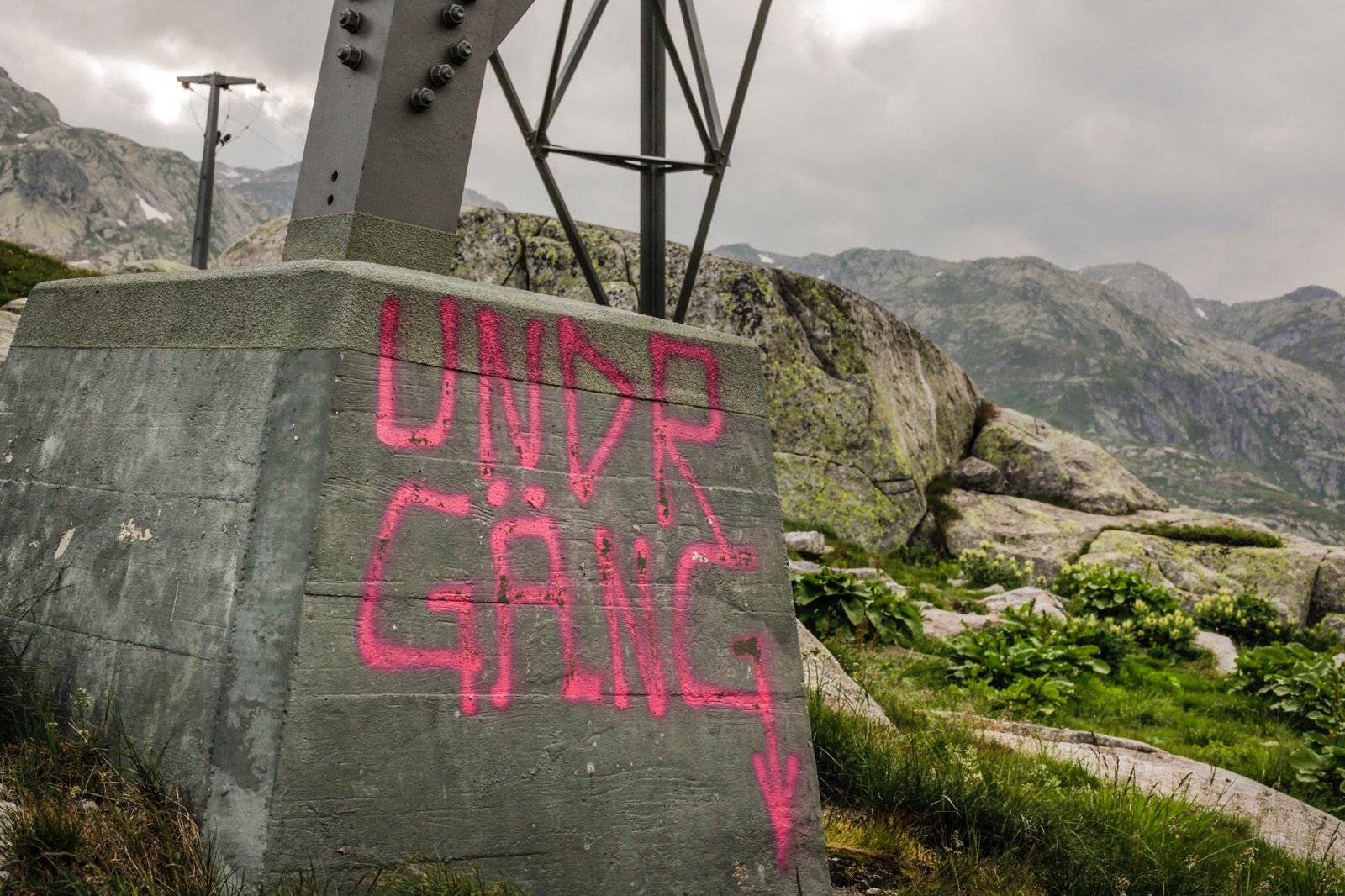 foto van een betonblok voor telefoonkabels bij de Gotthard pass in Zwitserland die met graffiti is beklad met op de achtergrond bergen