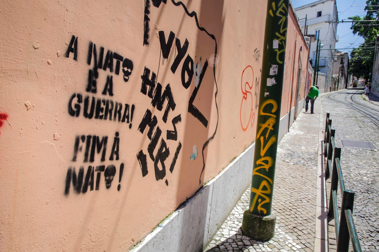 foto van een muur in Lissabon met graffiti en een stuk straat waar een man in een groen shirt kreupel loopt