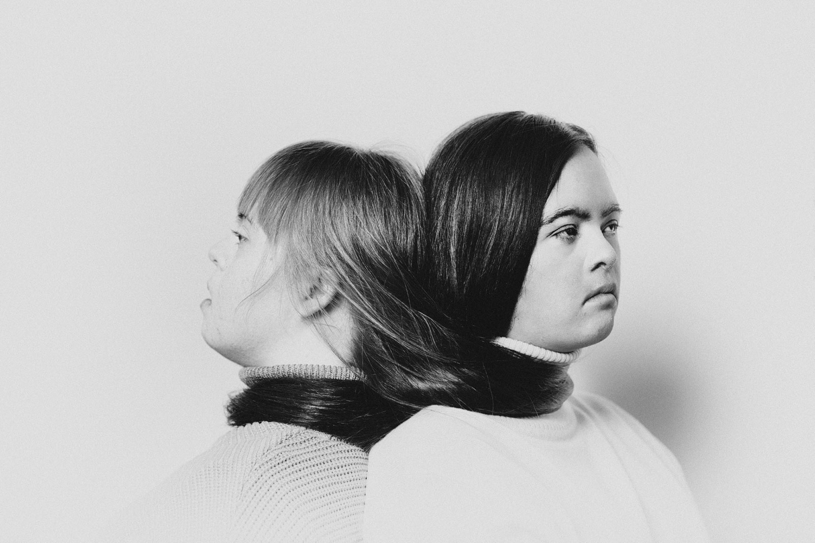 foto van twee vrouwen met down syndroom die met hun ruggen tegen elkaar aan zitten en hun haar om elkaar heen hebben