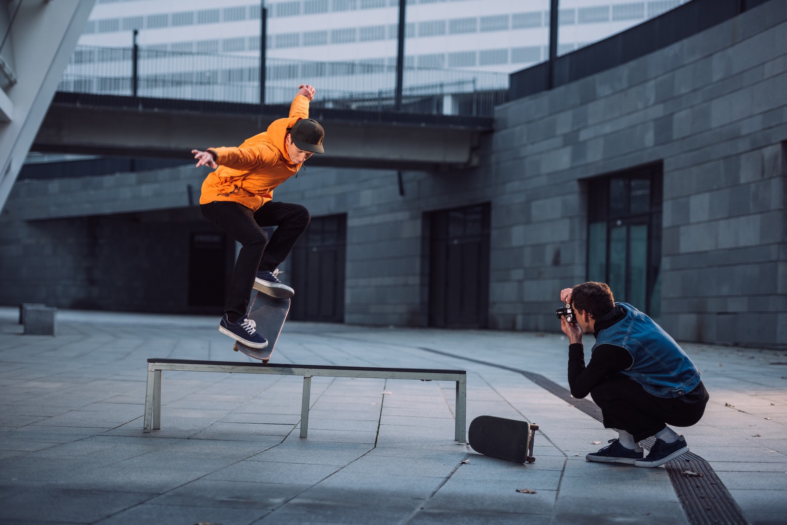 foto van een fotograaf die een skater fotografeert die met zijn plank op een bankje balanceert