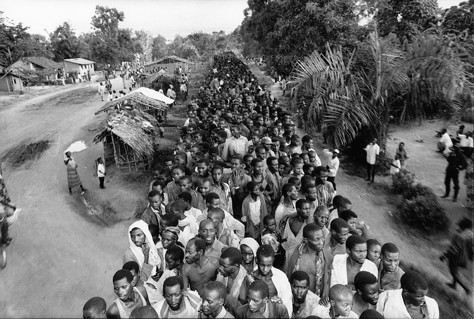 foto van een rij arbeiders in Rwanda in een bos met hutten