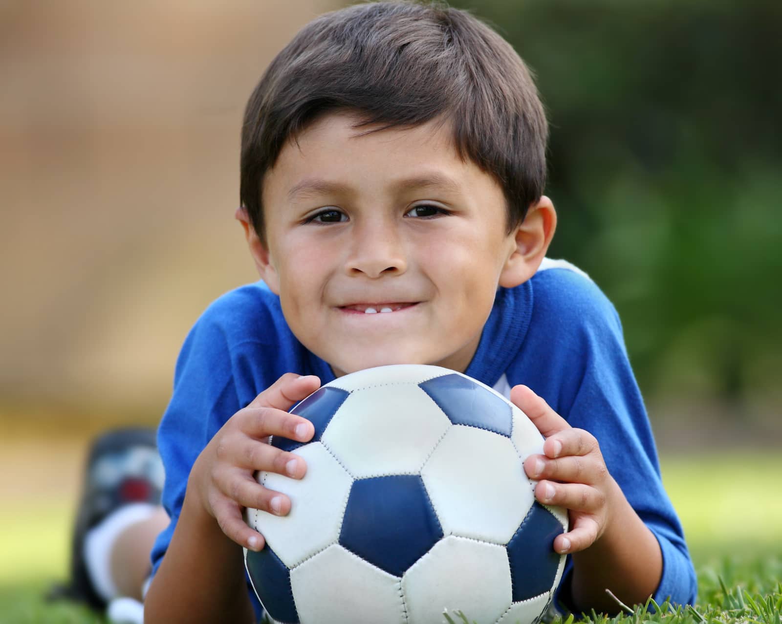 jongen liggend op buik met voetbal onder kin