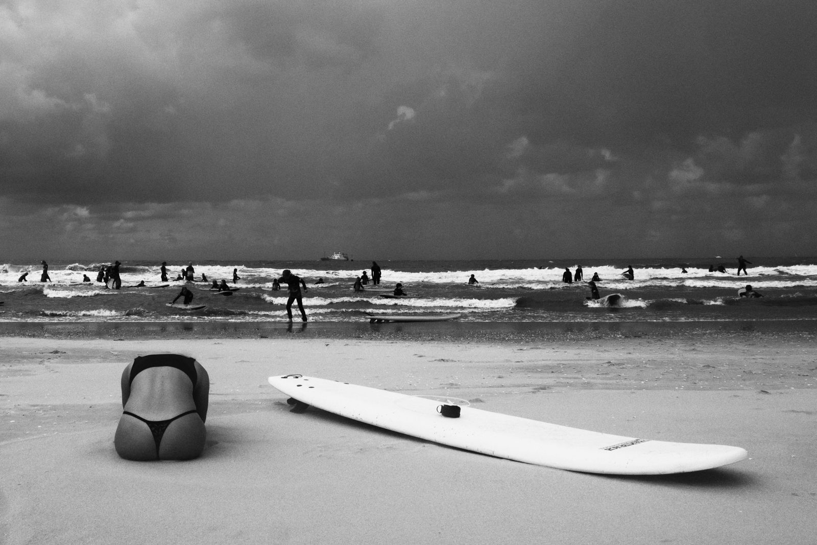 Foto van Merel Schoneveld van strand in zart wit met mensen in branding en op zand ligt surfboard en een vrouw in yoga houding