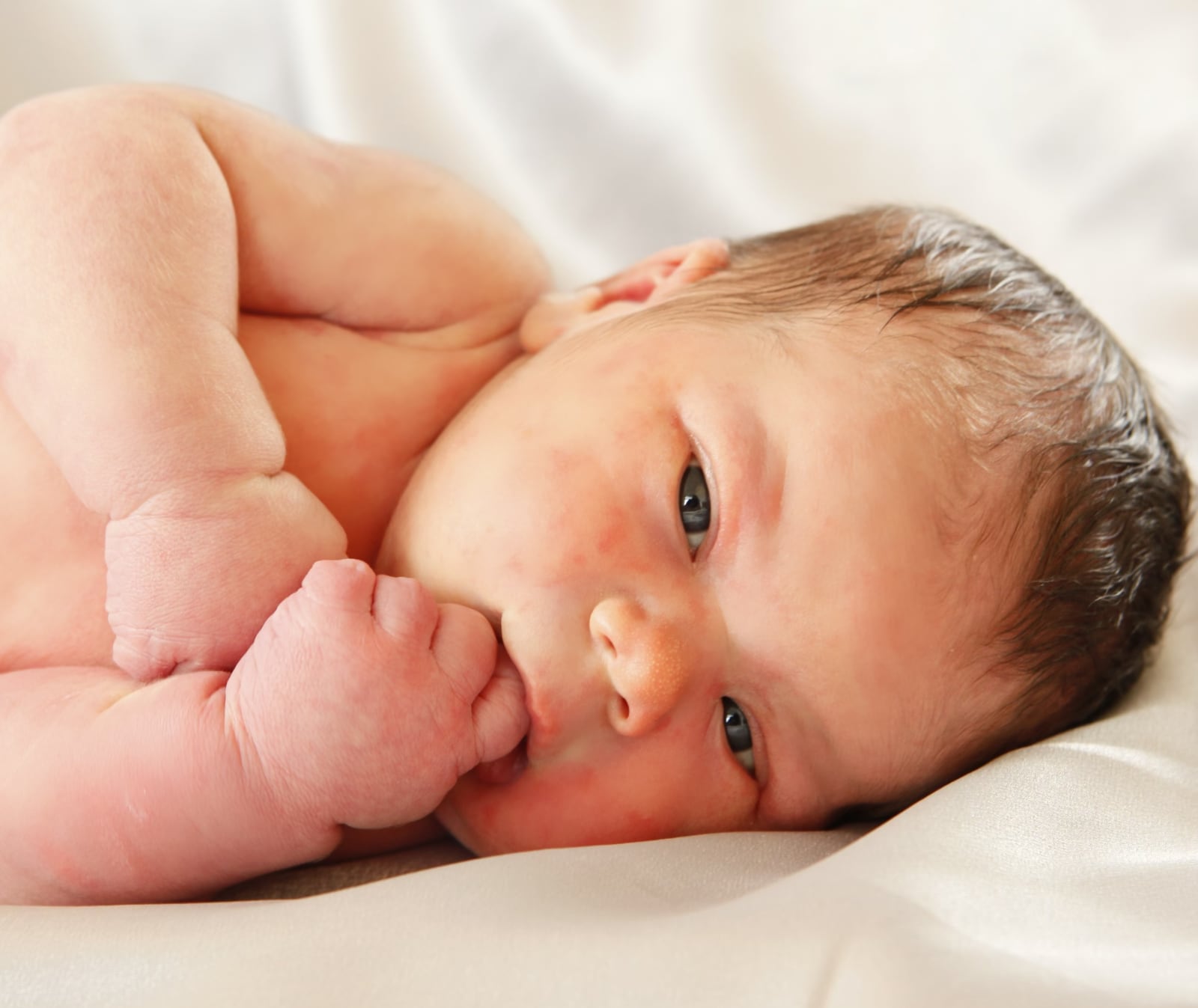 pasgeboren baby ligt op zij met vingertje in zijn mond door fotograaf Alex de Smit