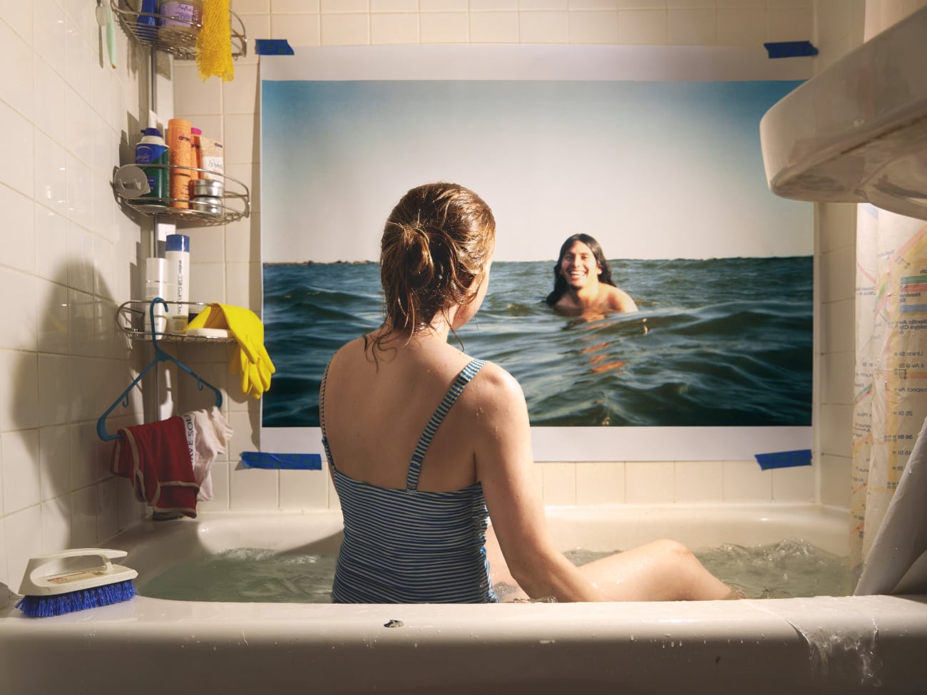 foto: © Alison Luntz - In Spirit - That Sunny Day: vrouw zit in bad en kijkt naar foto van vrouw die in zee zwemt