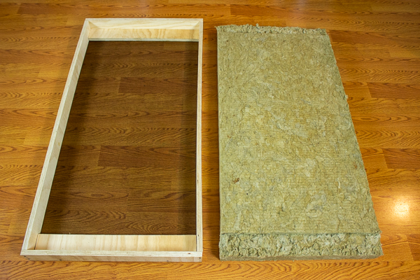 An image of insulation cut to fit inside an acoustic panel frame containing two support strips.