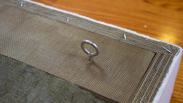 A close up view of a screw eye hook installed into the back of an acoustic panel.