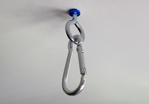 An image of a carabiner that has been clipped onto a screw eye hook and screwed into a drywall anchor in the ceiling.