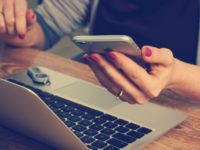 woman checking phone and typing on laptop