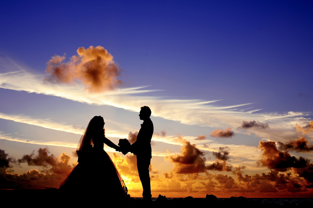 a bride and groom stand silhouetted against a dramatic blue and orange sunset over the ocean