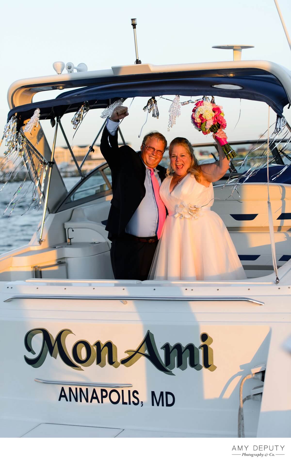 a bride and groom wave from a boat called mon ami from annapolis mar