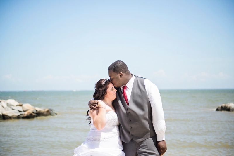 A groom leans over to kiss his bride in front of the sea at mayo beach park in marlyand