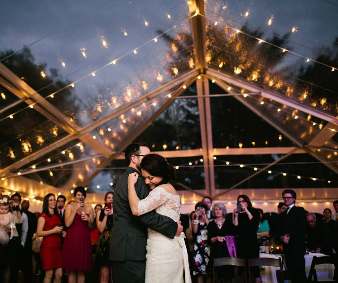 a bride and groom dance together surrounded by friends and family under twinkling lights