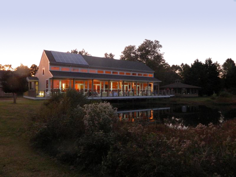 a building on a small pond is aglow in the fading light
