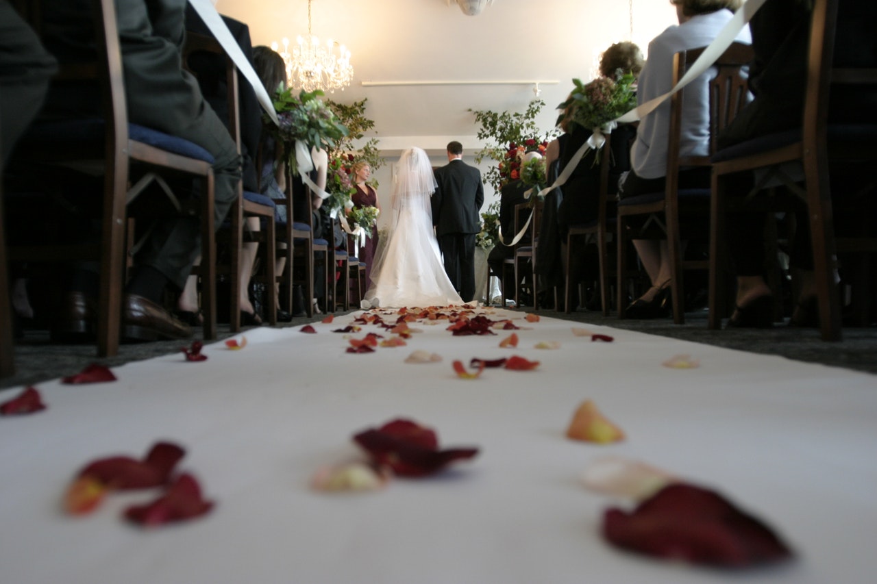 petals along the aisle of a church as a bride and groom stand at the altar