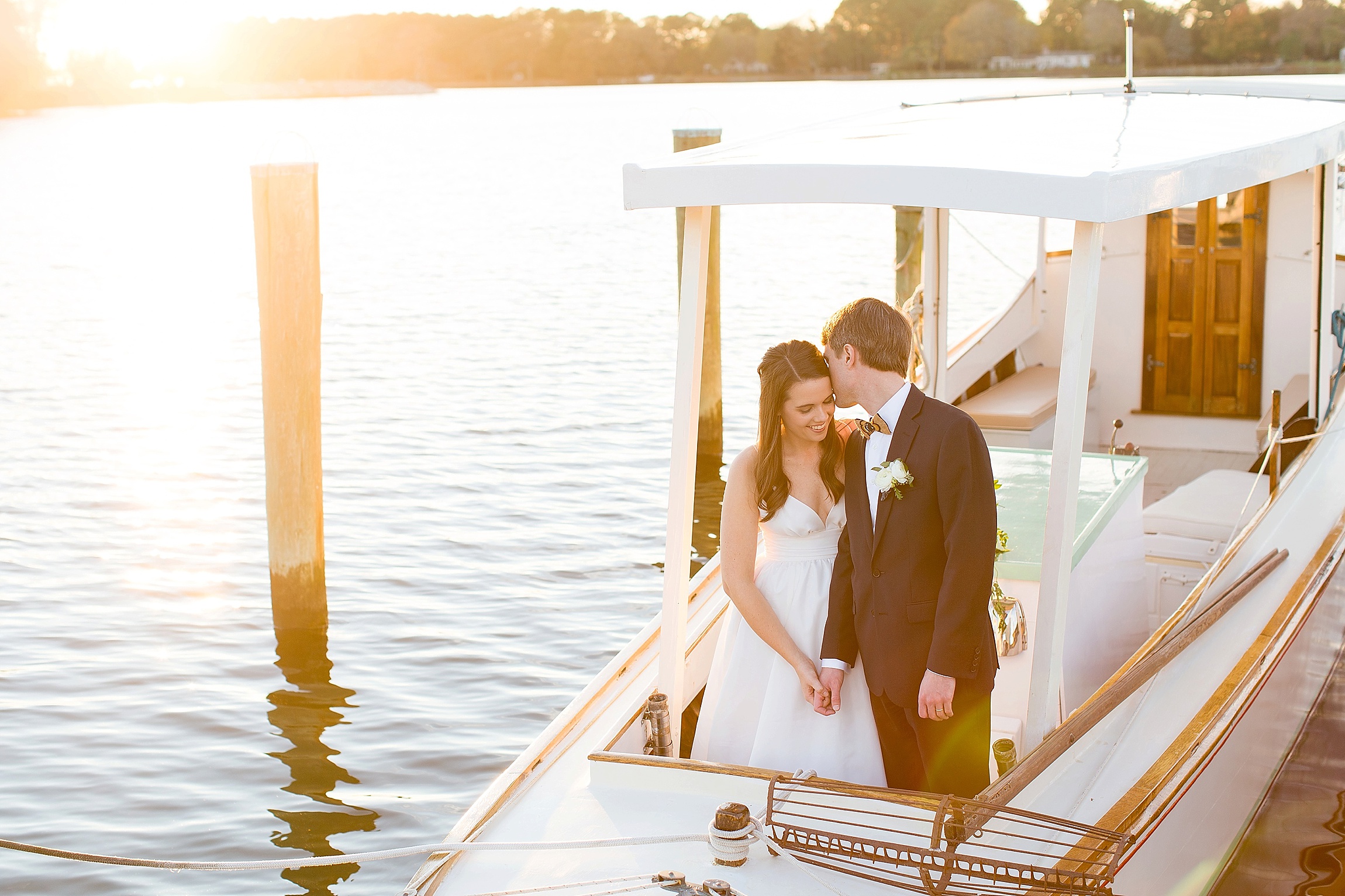 a bride and a groom kiss on a small boat at sunset