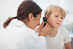 Audiologist examining child's ear with an otoscope