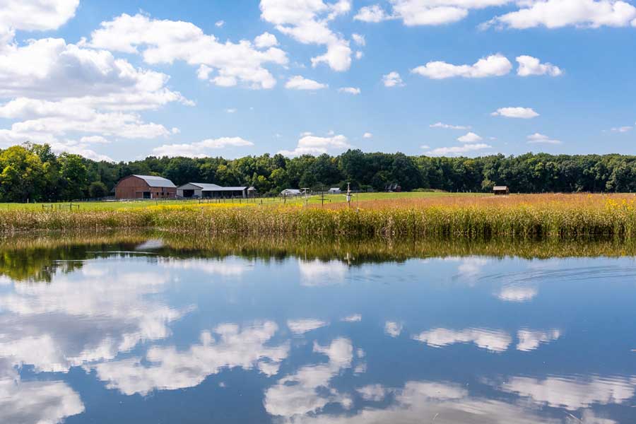 blue lake with field, farm, and forest in the background