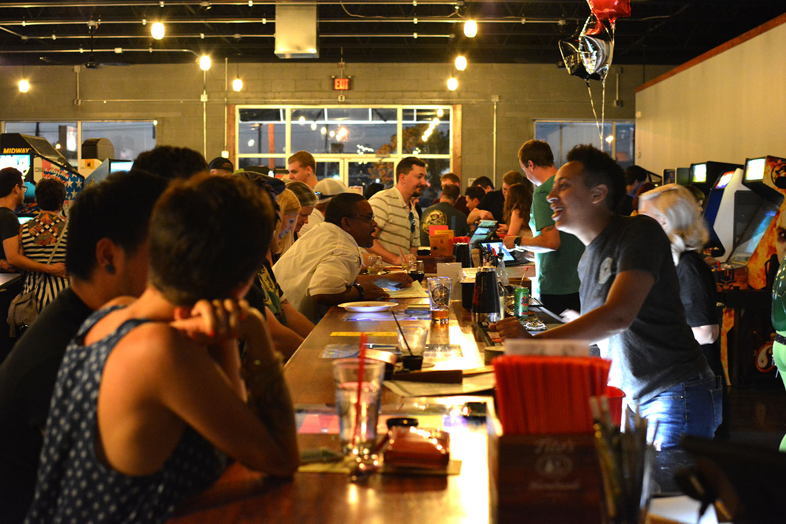 people drinking at bar in DK Effect with arcade games in background