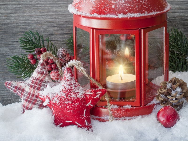 An old fashioned red lantern sits in a snowdrift surrounded by decorative pinecones and berries.