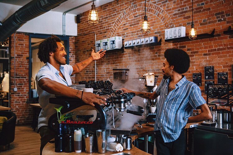 Stylish barista and customer interacting in front of brick wall in coffee shop setting