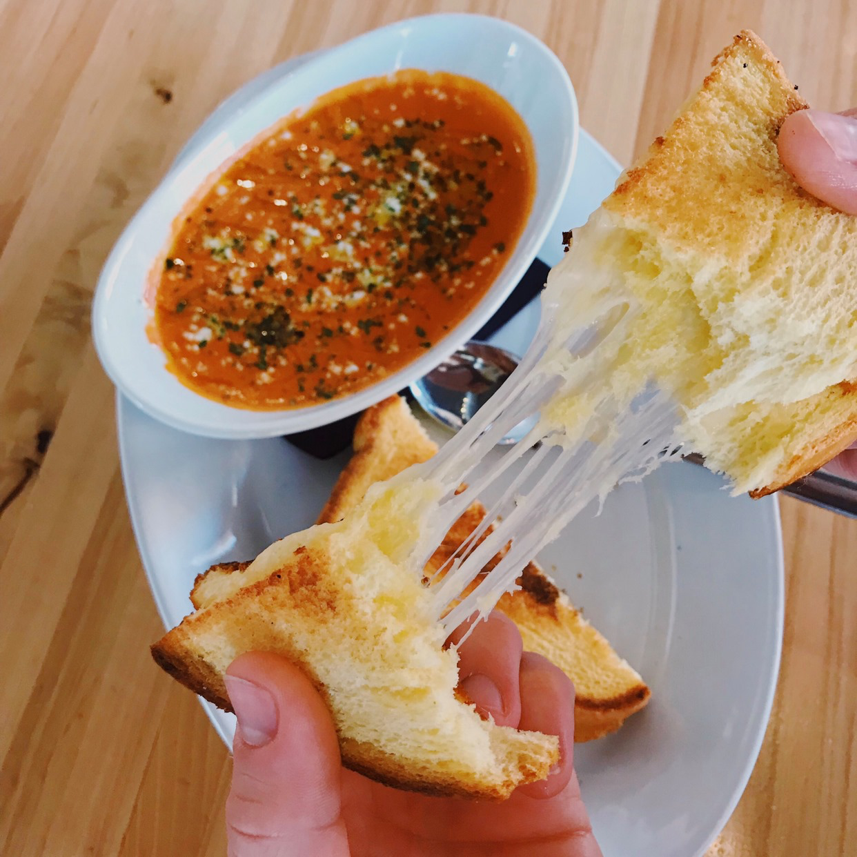 Gooey grilled cheese ripped above a bowl of bright red tomato soup